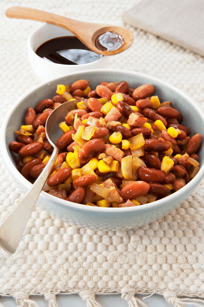 kom met bruine bonen met spek en ui, maïs en een lepel stroop.