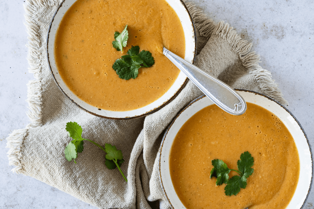 Twee kommen linzen curry soep op een beige linnen servet met verse koriander en een zilveren lepel.
