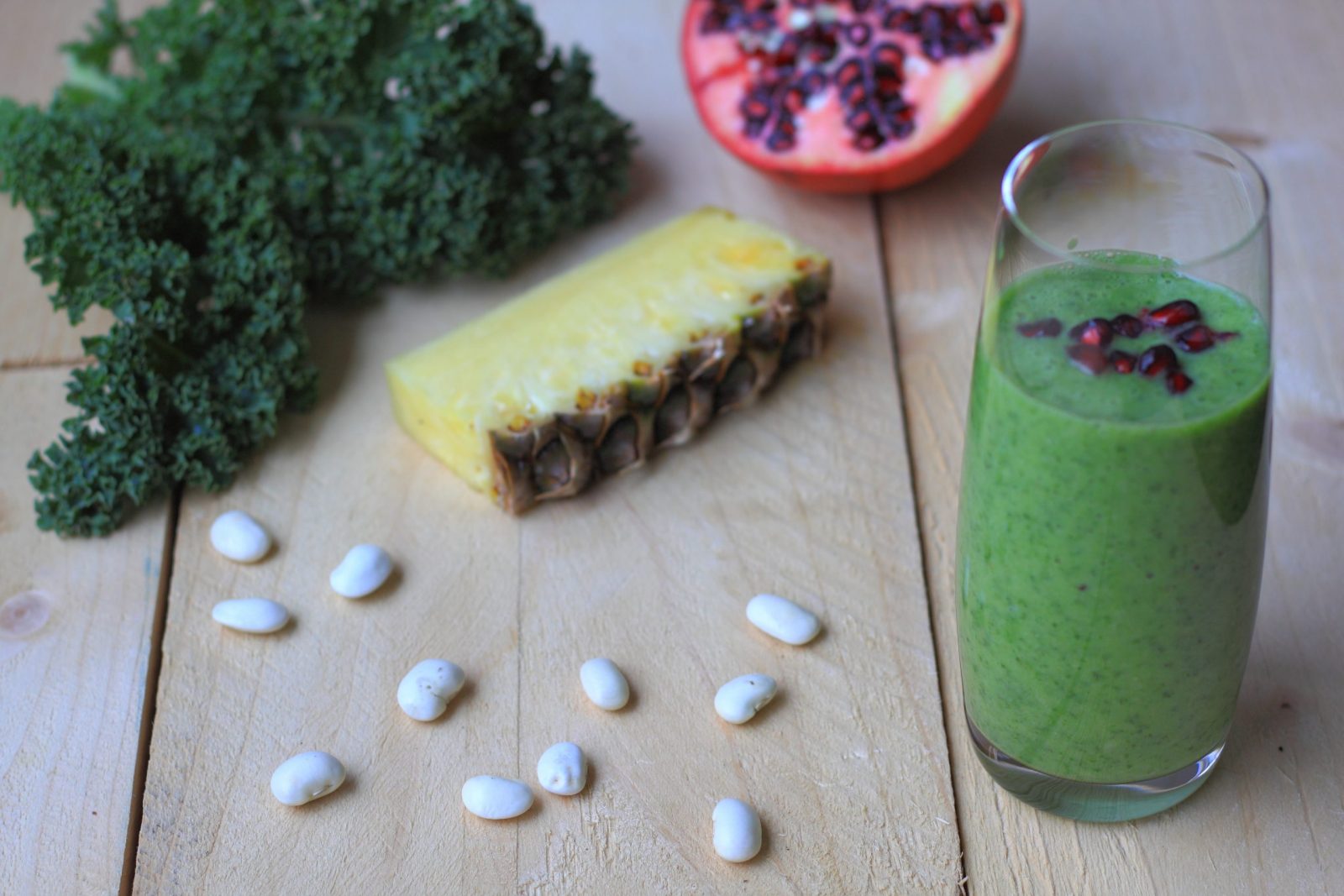 gezonde groene smoothie met boerenkool, ananas en granaatappelpitjes op een houten tafel.