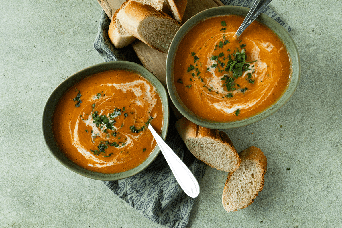 Twee kommen huisgemaakte rode linzensoep met wortel, een swirl van room en verse peterselie, geserveerd met brood.