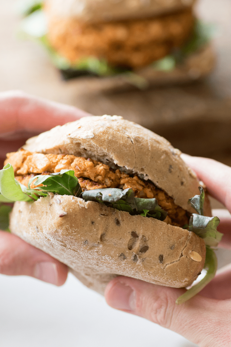 Close-up van een hand die een bruine bonenburger vasthoudt met sla op een volkorenbroodje