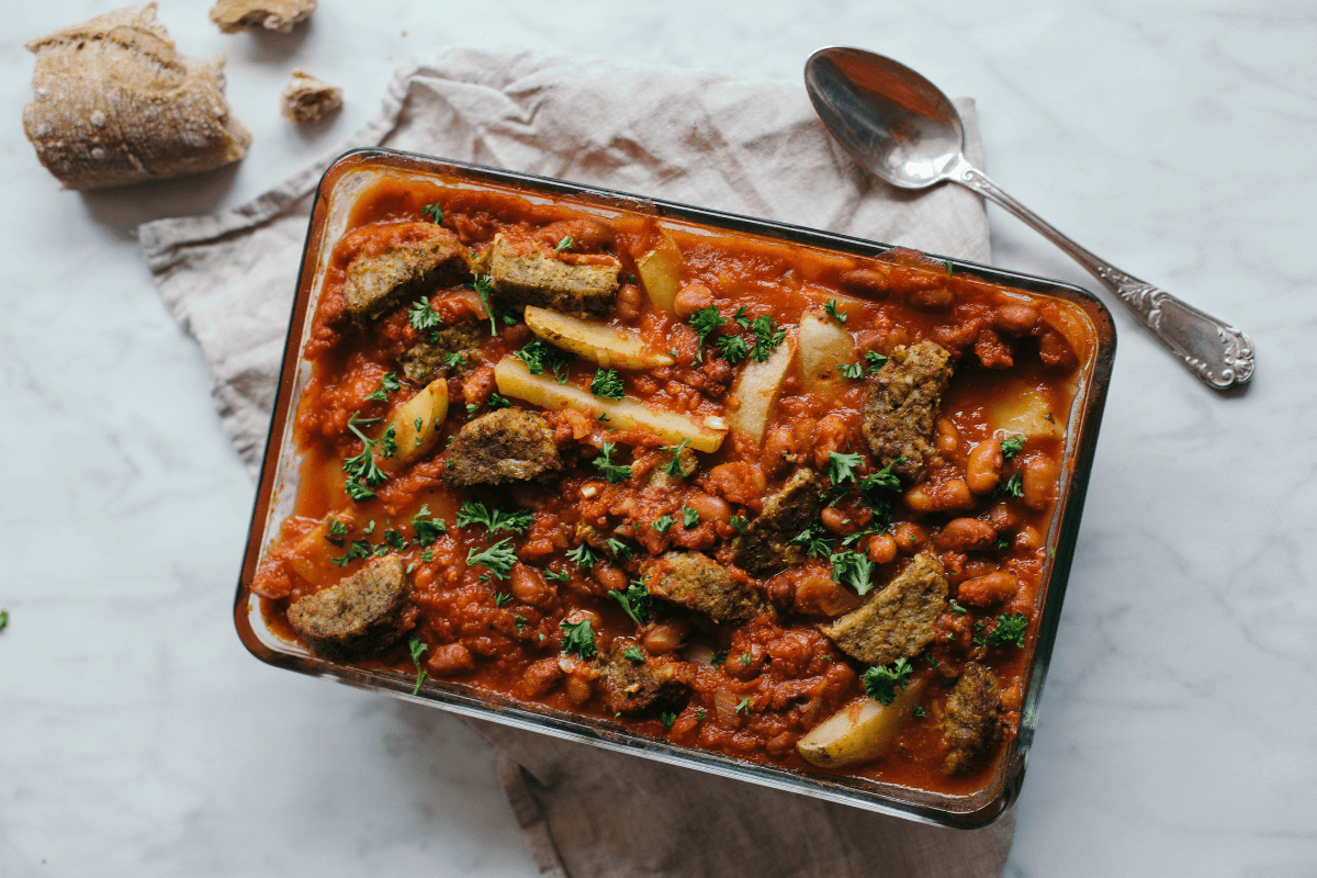 Glazen ovenschaal gevuld met vegetarische bruine bonen schotel met aardappelen en stukjes vleesvervanger, gegarneerd met peterselie.