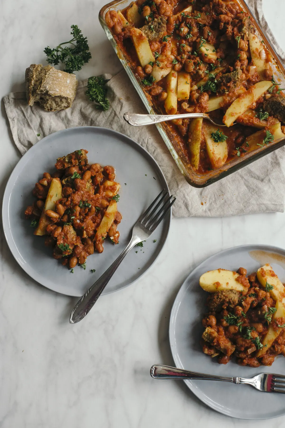 Grote glazen ovenschaal met rijke vegetarische bruine bonen schotel met vleesvervanger, aardappel en tomatensaus.