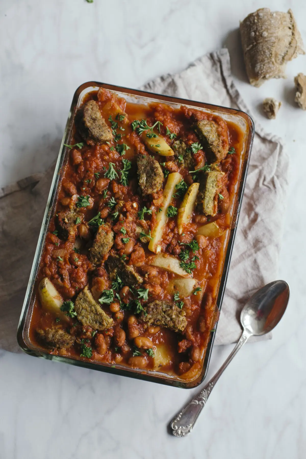 Glazen ovenschaal met vegetarische bruine bonen schotel, stukjes aardappel en vleesvervanger, gegarneerd met peterselie.
