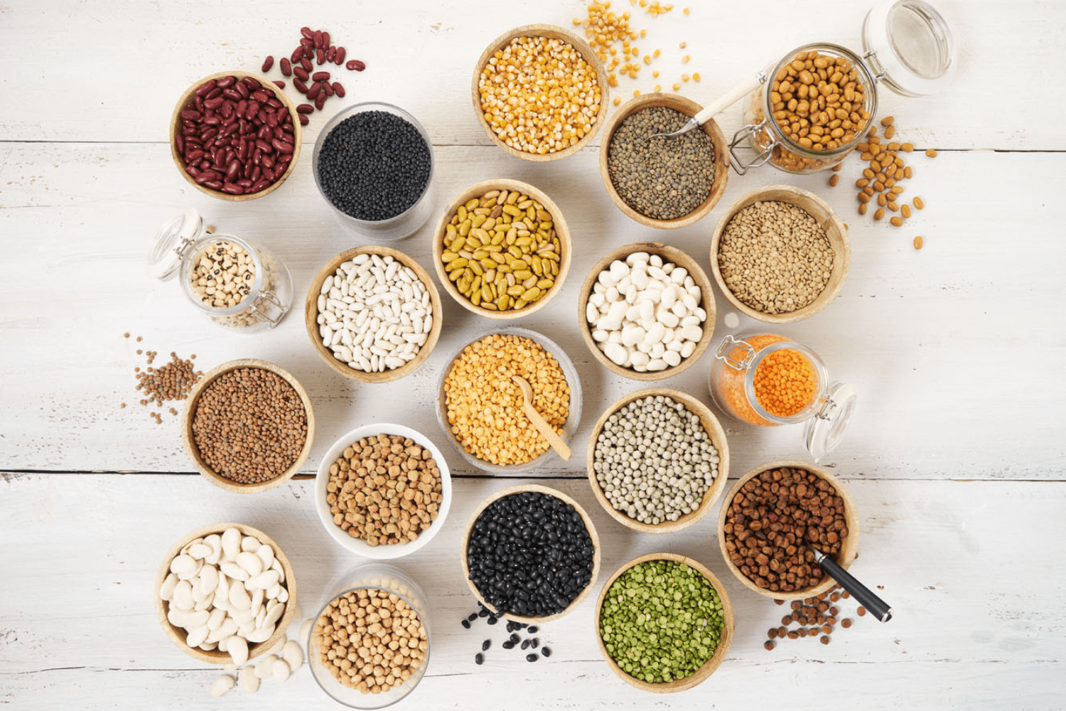 Verschillende soorten peulvruchten, zoals rode, groene en gele linzen, in houten kommetjes.