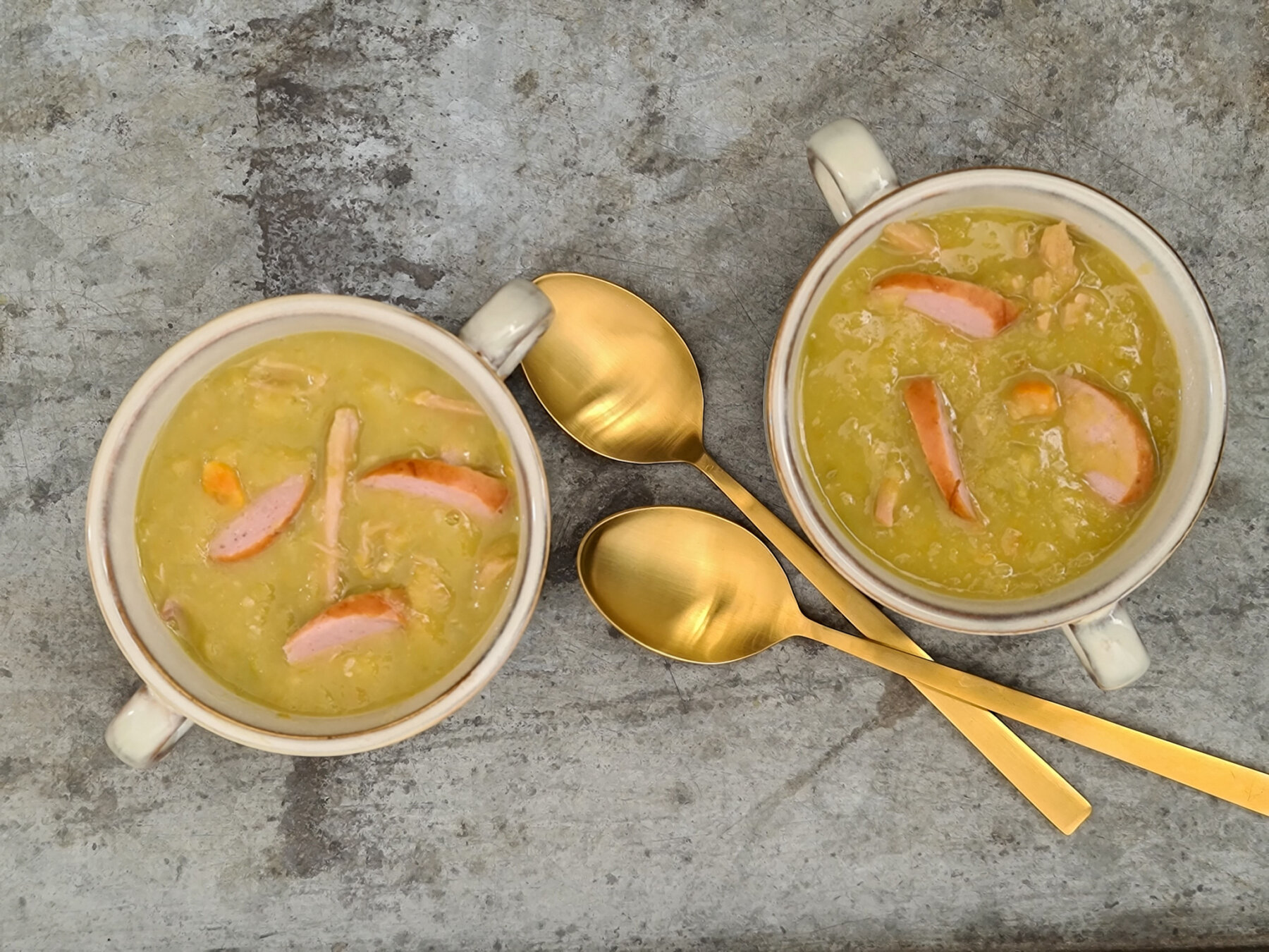 Twee kommen ouderwetse erwtensoep met rookworst en goudkleurige lepels
