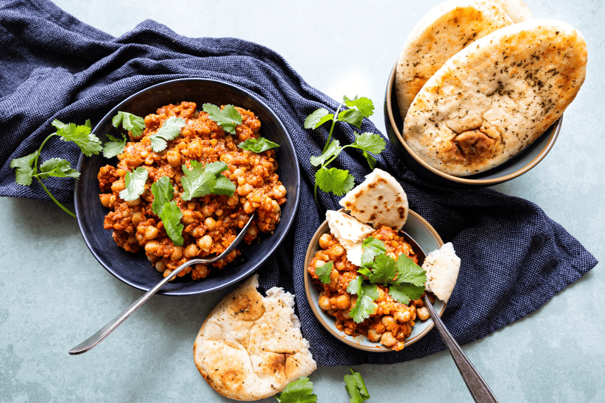 detail van een gezonde linzenstoof met kikkererwten en naan op een blauwe doek.