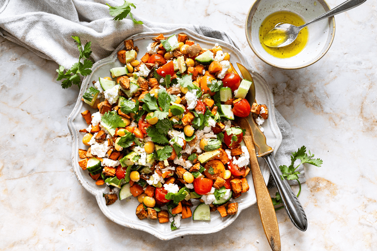 Lupinebonen salade met geroosterde zoete aardappel, feta, kerstomaatjes, komkommer en verse koriander op een sierschaal.